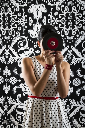 young woman looking through the hole of a small record with a red labelの写真素材