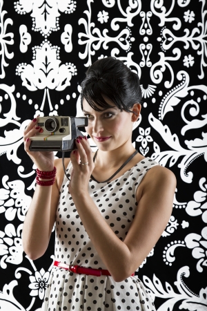 young woman is stylist 60's inspired clothing, holding an instant camera and preparing to take a photoの写真素材