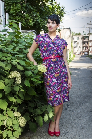 Young fashionable woman wearing a multi colored flower pattern dress near a flower bush in an urban alleyの写真素材
