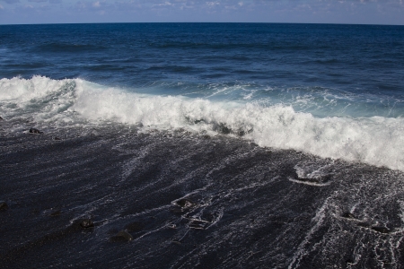 Wave crashing on a black sand beach in Hawaiiの写真素材