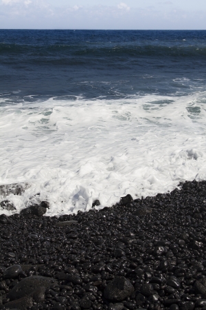 Black stone beach shore on the Big island of Hawaiii being pounded by waveの写真素材
