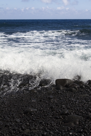 Black stone beach shore on the Big island of Hawaiii being pounded by waveの写真素材
