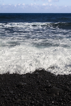 Black stone pebbles being pushed wave, on the beach shore, on the Big island of Hawaiiiの写真素材