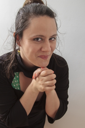 Woman wearing a black dress with wispy flowing hair holding her hand in praying position and mischievous smileの写真素材