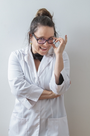 thirtie something brunette woman wearing a lab coat holding her glasses with a big funny smileの写真素材