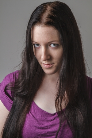 young woman with long black hair and a purple shirt, with her head down and looking up from the corner of her eyesの写真素材