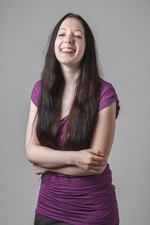 young woman with long black hair and a purple shirt laughing, holding her stomach and sticking out her tongueの写真素材