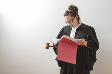 thirty something brunette woman wearing a canadian lawyer toga with a gavel in her hands and reading...
