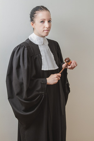 twenty something woman wearing a canadian lawyer toga, banging a gavel in her hand and giving the evil eyeの写真素材