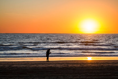Fisherman on a beach about to throw his line in the ocean at sunsetの写真素材