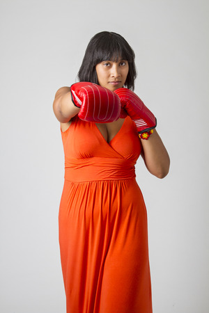 twenty something philipino woman, in low cut orange dress, throwing a punch with red boxing glovesの写真素材