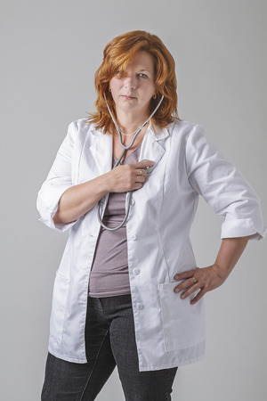Woman wearing a lab coat and putting a stethoscope in her heartの写真素材