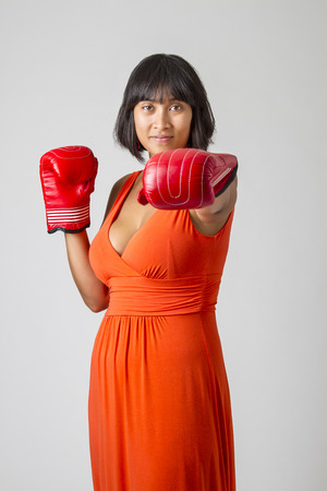 Young sexy philipino woman, wearing a low cut orange dress, throwing a punchの写真素材