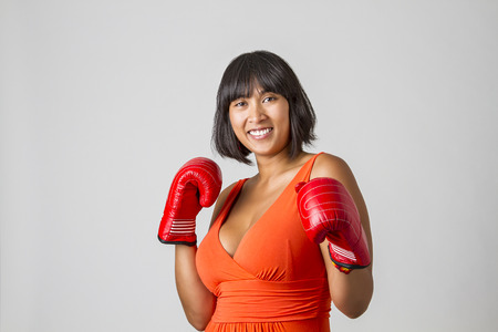twenty something asian woman wearing a low cut orange dress with great smile gearing up for a punchの写真素材