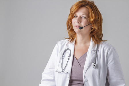 forty something woman doctor with red hair with a stethoscope and a headsetの写真素材