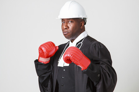 Mid-forties bald black man wearing a canadian lawyer toga, white hard hat, stethoscope and boxing boxing gloveの写真素材