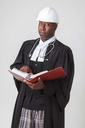 Men with hard hat, stethoscope in a lawyer toga holding a red law bookの写真素材