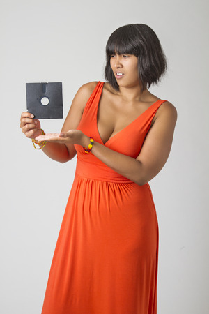 Philipino woman wearing a low cut orange dress pointing at a five inch floppy drive looking disturbの写真素材