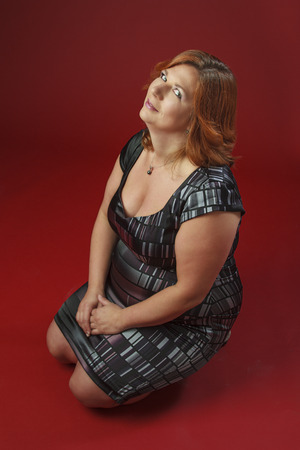 Woman in her fortie, wearing a cocktail dress, sitting on her kneesの写真素材