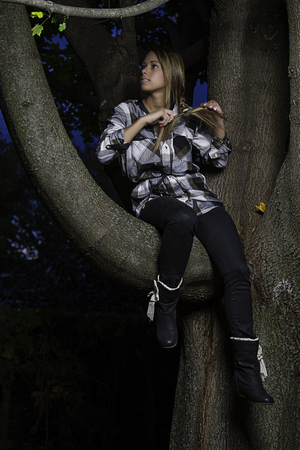 twenty something girl sitting on a tree branch tying her hairの写真素材