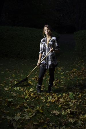 woman in her twenties raking leaves at nightの写真素材