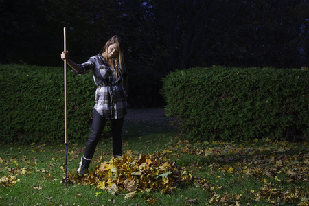 twenty something girl holding a rake and looking at a small pile of leavesの写真素材