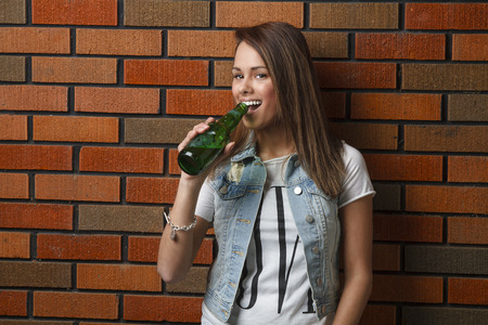 twenty something girl leaning against wall drinking a beerの写真素材