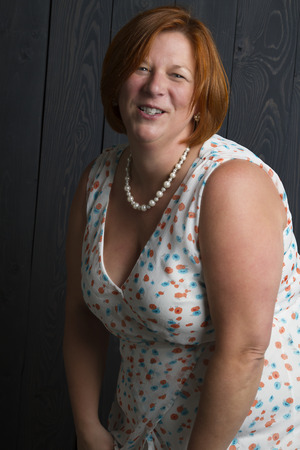 forty something overweight woman wearing a summer dress in front of a blue wood stain backgroundの写真素材