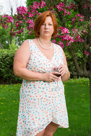 forty year old woman in summer dress, having a glass of wine under a cherry treeの写真素材