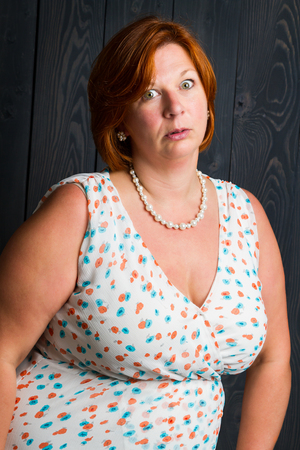 forty something brunette woman wearing a sun dress in front of blue wood panel with annoyed expressionの写真素材