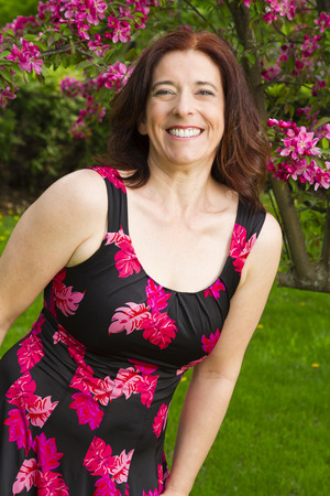 forty something brunette woman, wearing a summer dress, in front of a cherry treeの写真素材