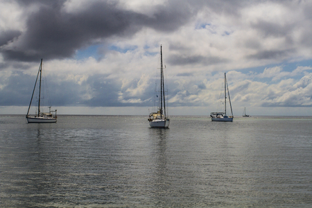 three sail boat on the ocean during a cloudy dayの写真素材