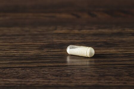 close-up of a transparent pill filled with white powder against a dark wood backgroundの写真素材