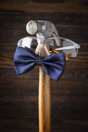 Old weather hammer wearing protective glasses and a blue bowtie against a dark wood backgroundの写真素材