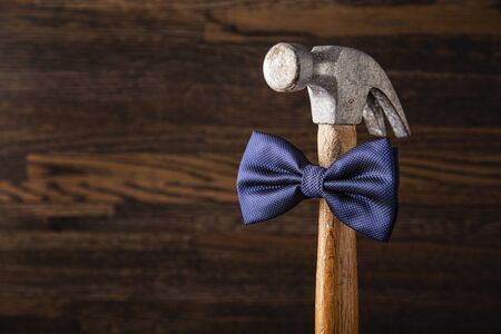 Old banged up hammer with a blue bowtie against a wood backgroundの写真素材