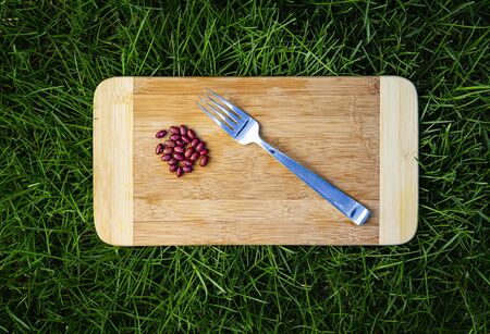 Red kidney beans and a fork, on a wood cutting board, in green grassの写真素材
