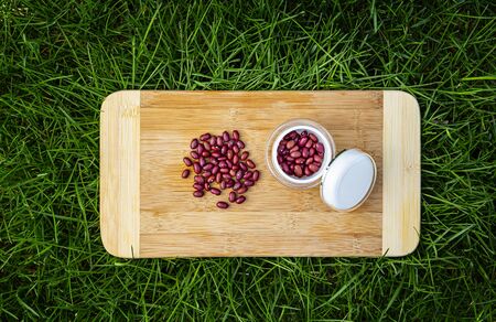 pile of red kidney beans on a wood cutting board, in green grass and small beauty cream container filled with red kidney bean
の写真素材