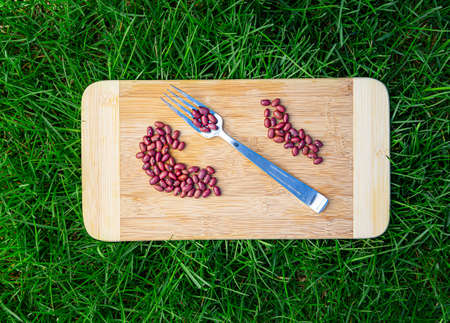 dried red bean, on a wood cutting board, with a metal fork, laying on top of green grassの写真素材