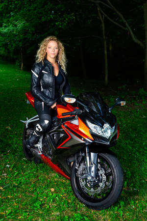 twenty something blond hair woman, wearing motocyle clothes, sitting on top of sport motocycle, in a parkの写真素材