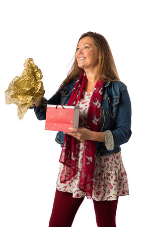Forty something woman, wearing casual clothes, opening a gift bag with a big smileの写真素材
