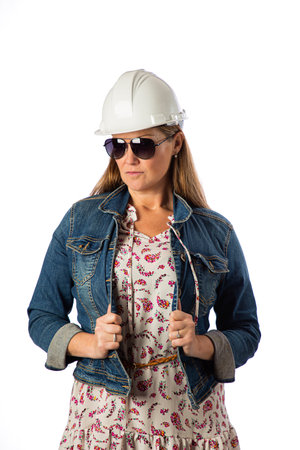 Forty something woman, wearing casual clothes, hard hat and sunglasses, holding her demin jacketの写真素材