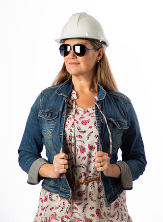 Forty something woman, wearing casual clothes, hard hat and sunglasses, holding her demin jacketの写真素材