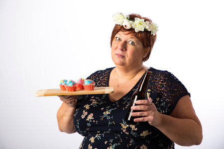 Fifty something woman with crown of flower, holding a bottle, offering a plate of cupcakesの写真素材