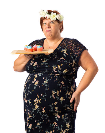 Fifty something woman holding a plate of colorful cupcakes, wearing a flower crown, with exhausted expressionの写真素材