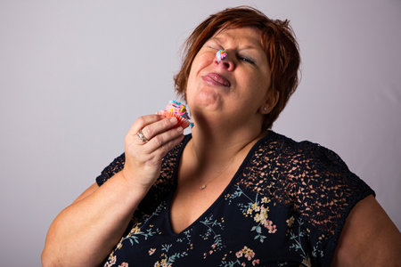 Fifty something woman with a colorful cupcake, with icing on her noseの写真素材