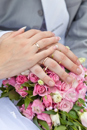 Hands of a newly-married couple with rings on a wedding bouquetの写真素材