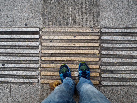 top view of man's feet or shoes on the sidewalk guides for blind. Yellow concrete cobblestones on...