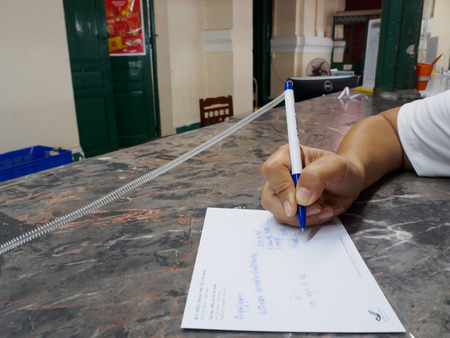 Woman writing recipient address on mailing envelope, female hands from above on office desk sending letterのeditorial素材