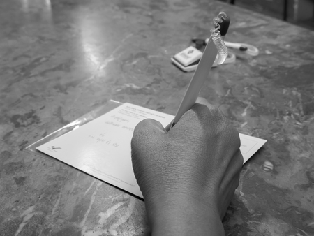 Woman writing recipient address on mailing envelope, female hands from above on office desk sending letter black and white pictureの写真素材