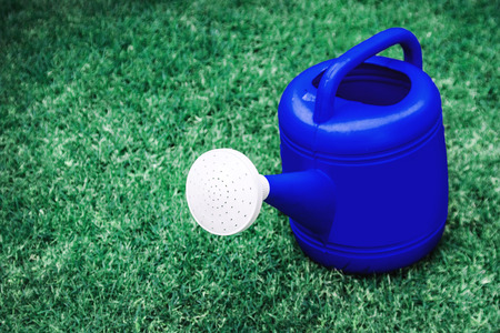 blue watering plastic pot on a green grass field in space in left hand の写真素材